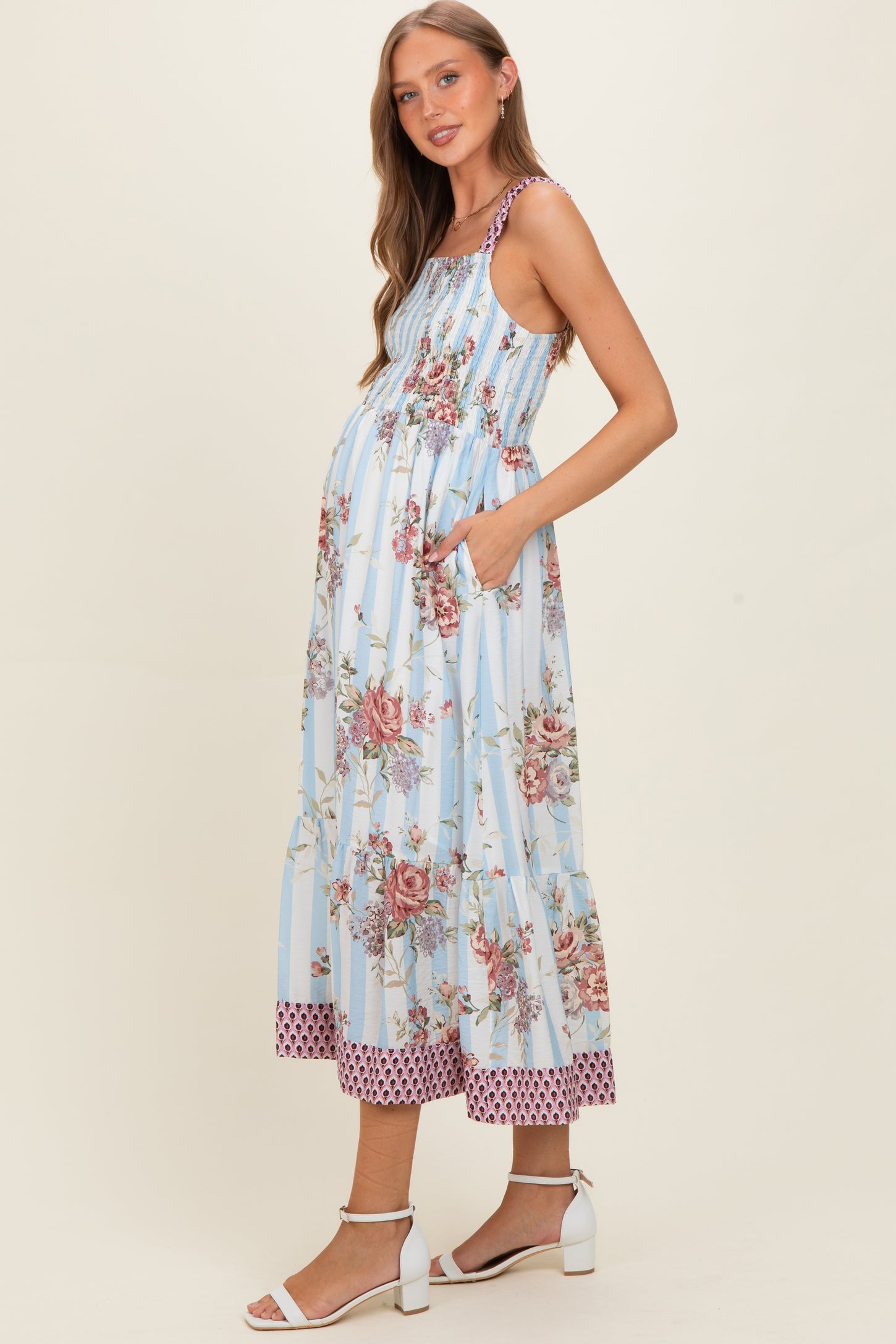 woman wearing a light blue floral maternity dress with pockets and a tiered hem, showcasing her baby bump