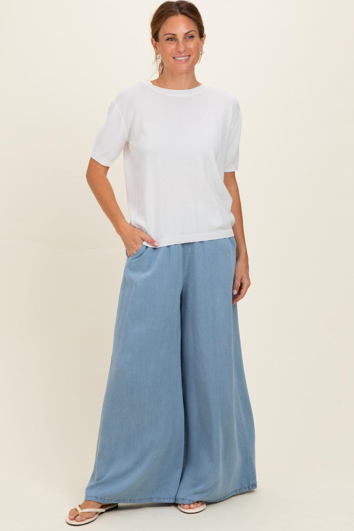 woman wearing a white short sleeve top and light blue wide-leg pants, standing with one hand in pocket