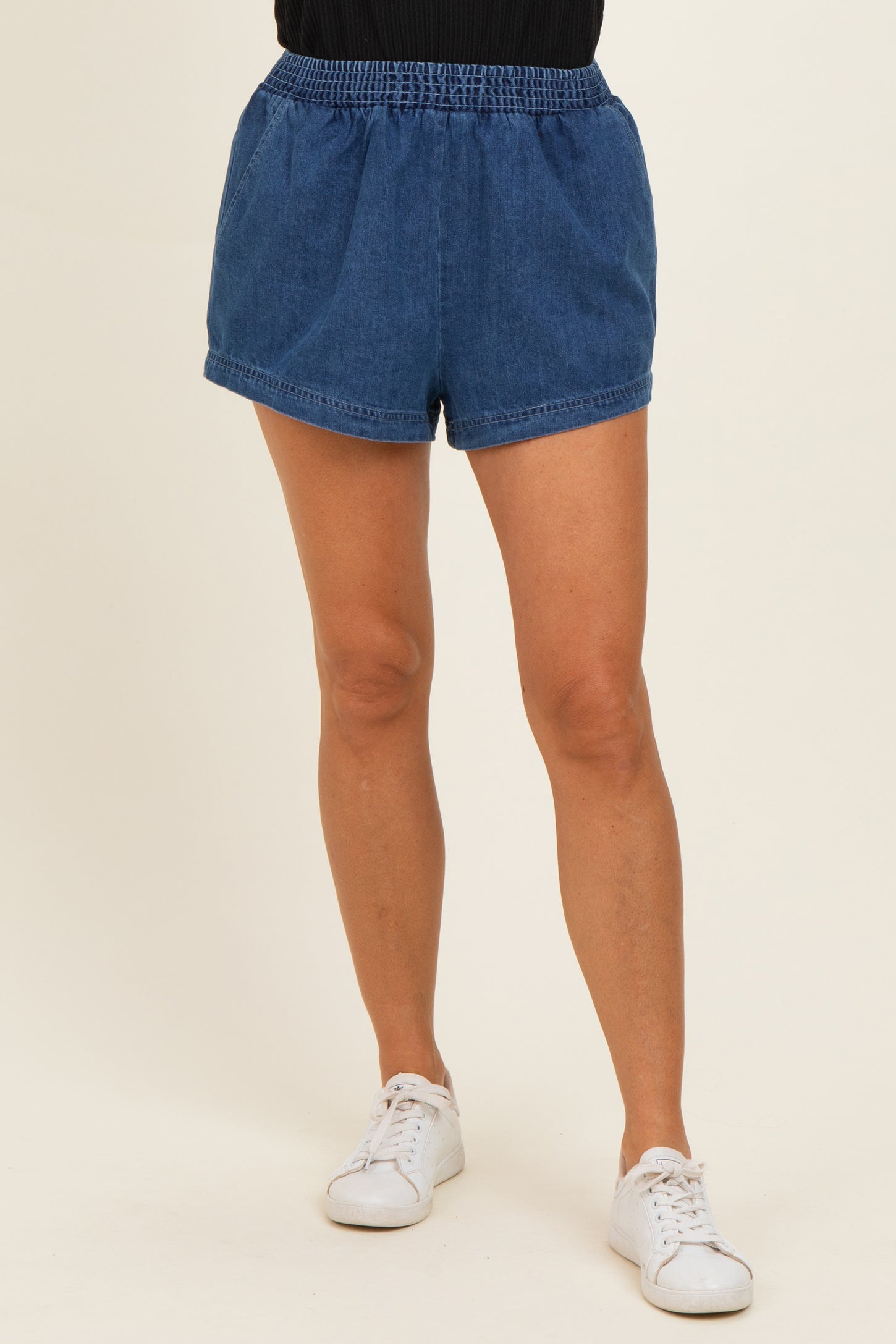 woman wearing blue denim shorts with an elastic waistband and side pockets, paired with white sneakers