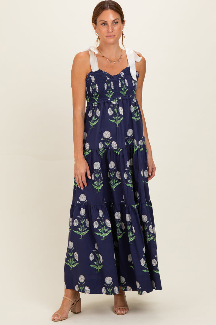 woman wearing a navy floral maxi dress with tie shoulder straps and a tiered skirt
