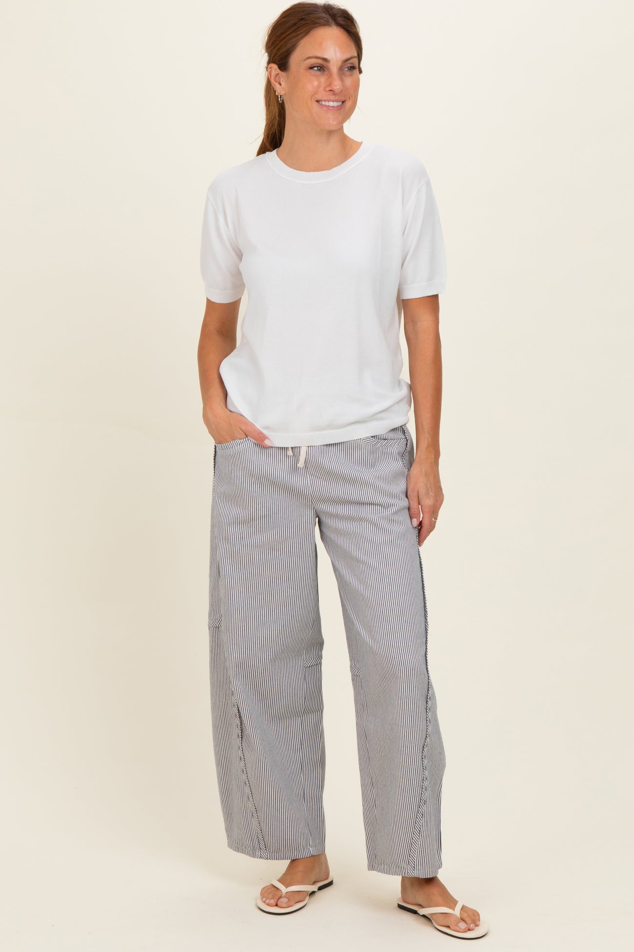 woman wearing a white short sleeve top and striped wide-leg pants, standing and smiling