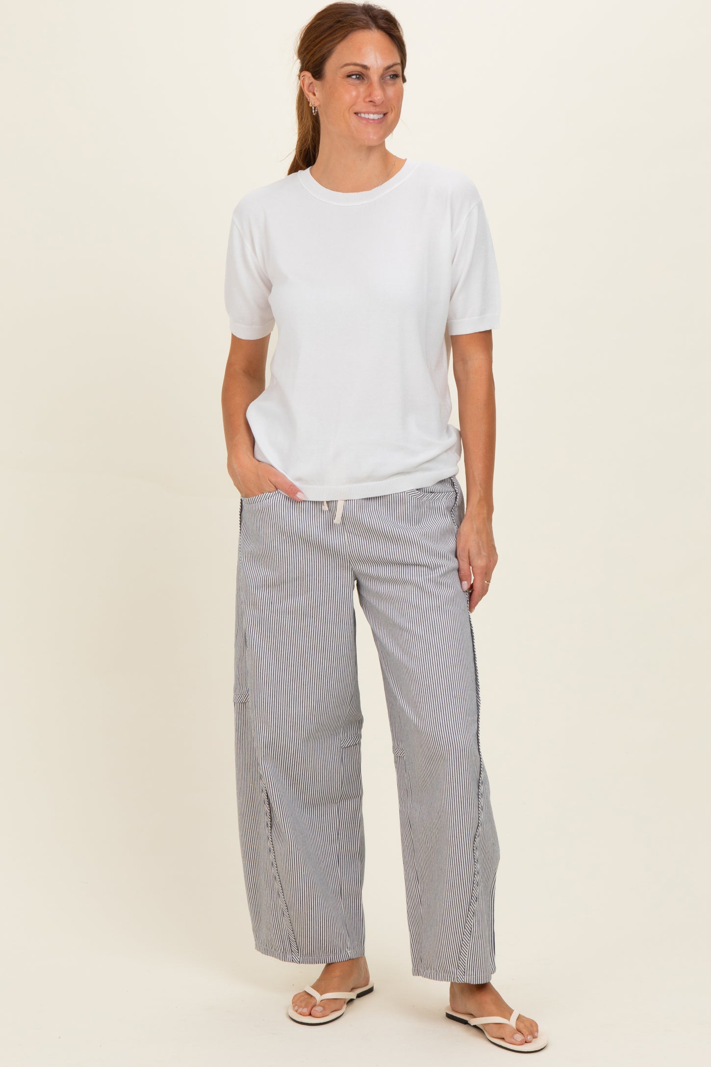 woman wearing a white short sleeve top and striped wide-leg pants, standing and smiling