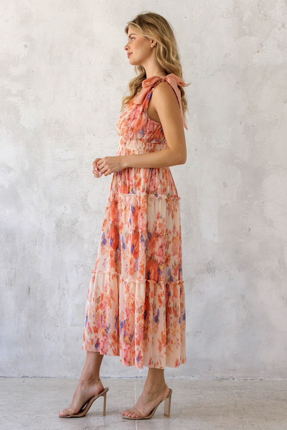 woman wearing a floral maxi dress with tiered layers and tie shoulder straps in soft peach and pink tones