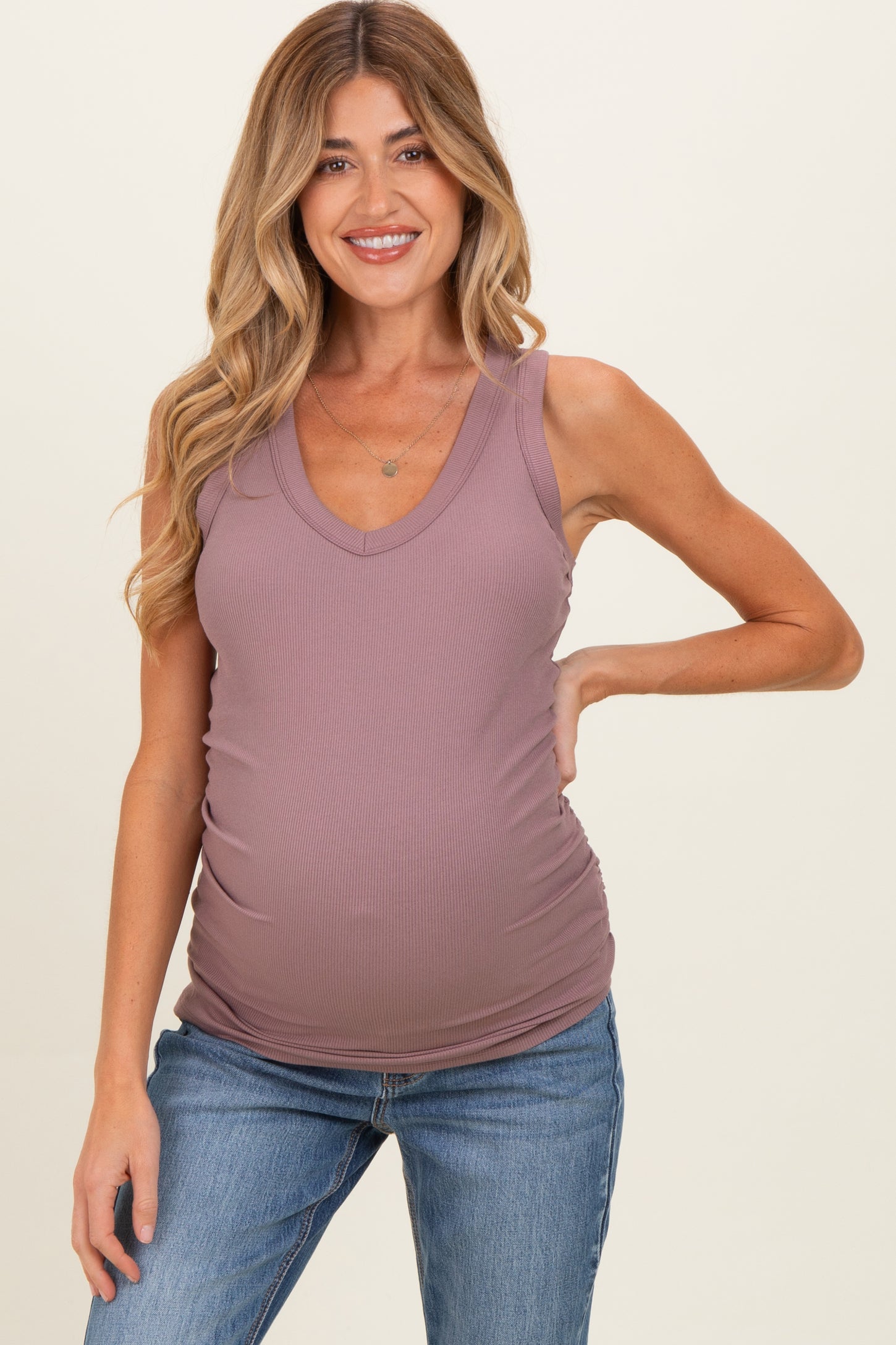 woman wearing a mauve maternity tank top with a v-neck and showing her baby bump while smiling