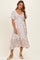 woman wearing a blush floral midi dress with short sleeves and a smocked bodice, standing against a neutral background
