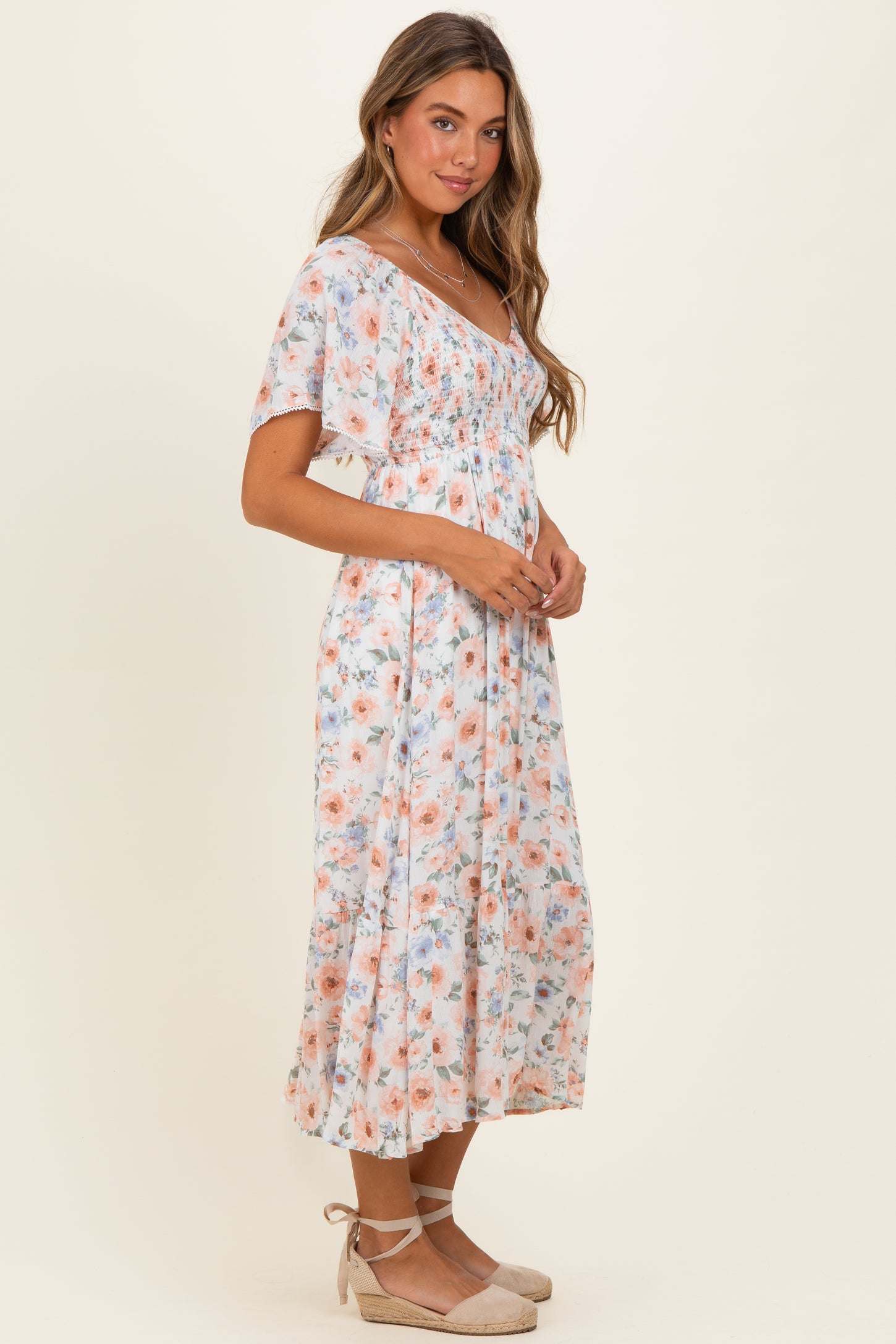 woman wearing a light floral midi dress with short sleeves and a fitted bodice, posing sideways with a smile
