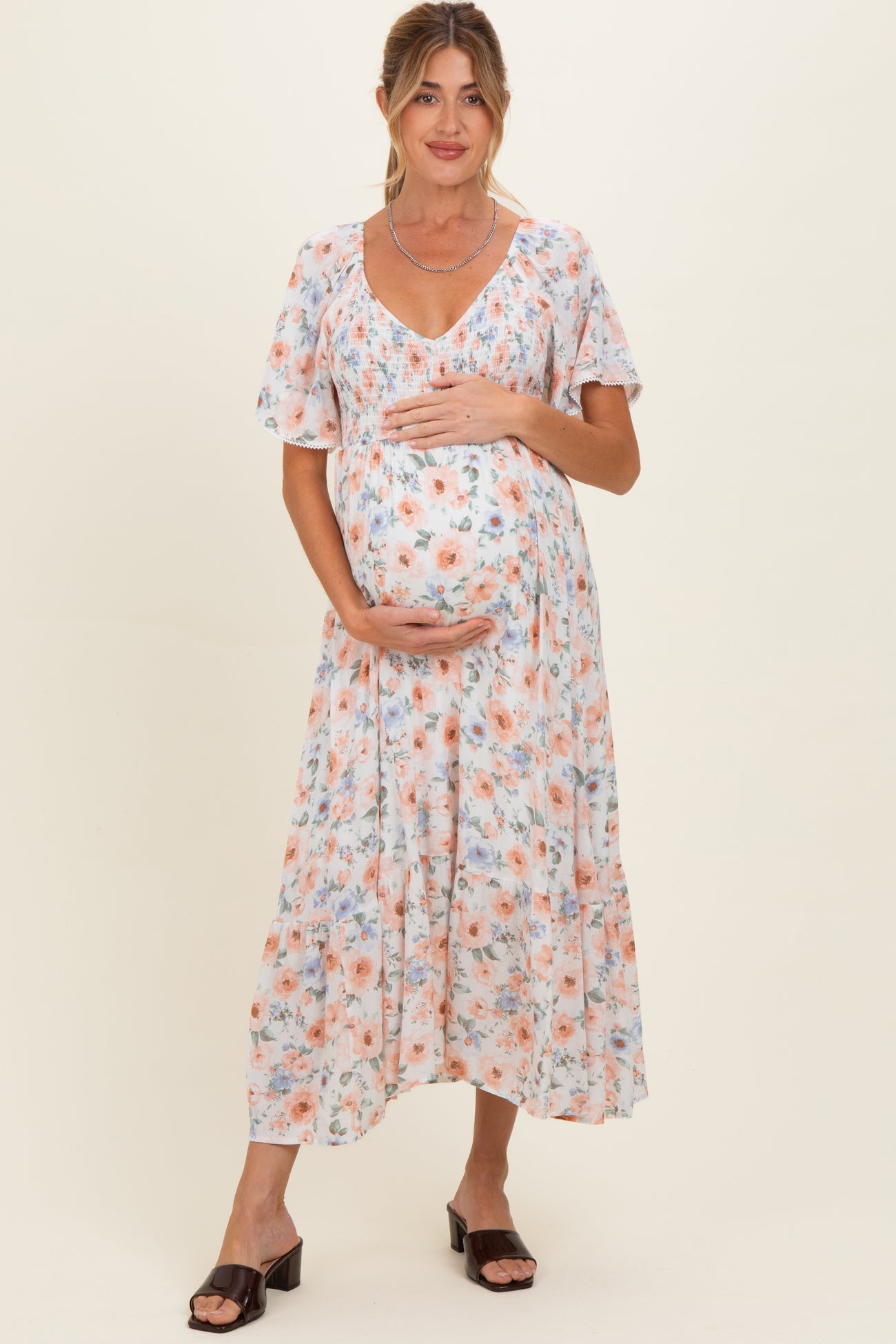 woman wearing a floral maternity dress with short sleeves, holding her baby bump