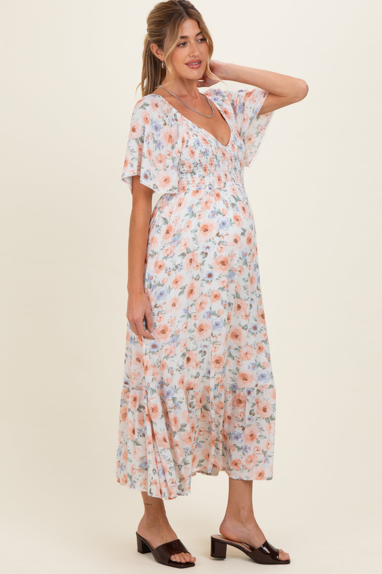 woman wearing a floral print maternity dress with a v-neckline and flutter sleeves, showcasing her baby bump