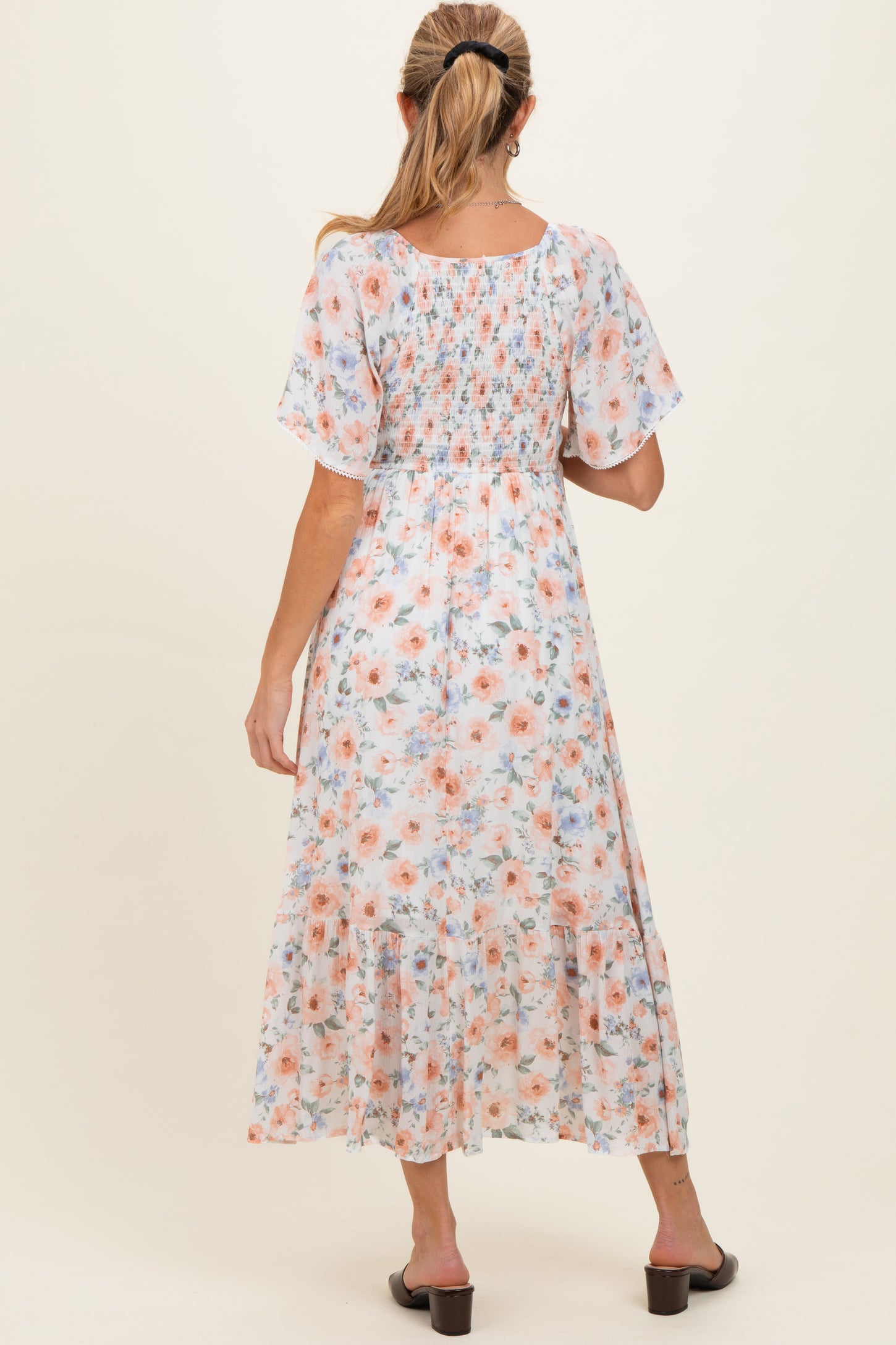 woman wearing a floral print maternity dress with short sleeves and a tiered hem, showcasing a baby bump