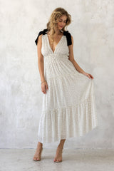 woman wearing a white polka dot maxi dress with a v-neckline and tiered skirt, standing against a textured background
