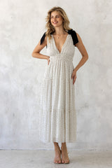 woman wearing a white tiered maxi dress with black tie straps and a plunging neckline