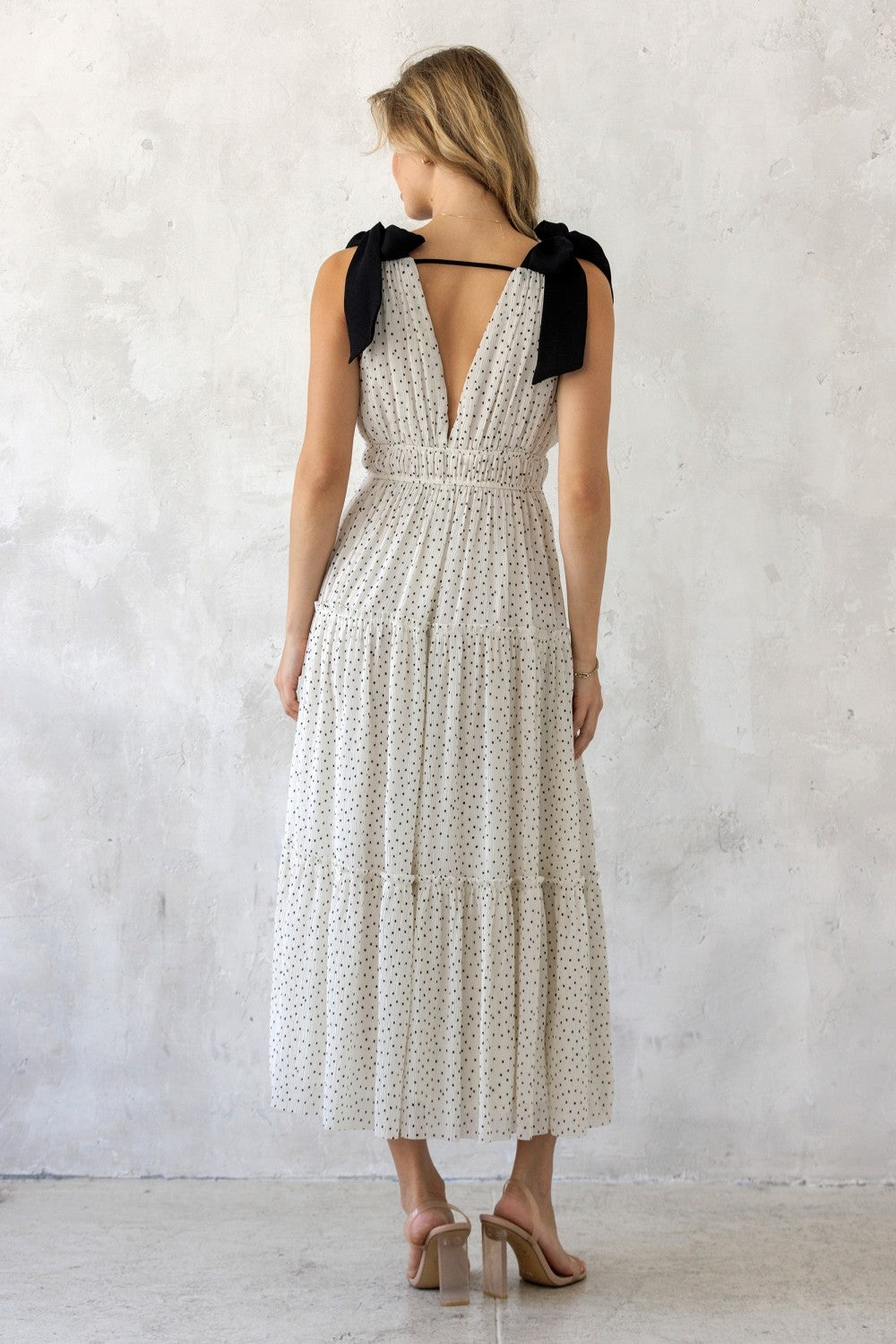 woman wearing a white polka dot maxi dress with black bow straps and a tiered skirt, viewed from the back