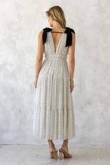 woman wearing a white polka dot maxi dress with black bow straps and a tiered skirt, viewed from the back
