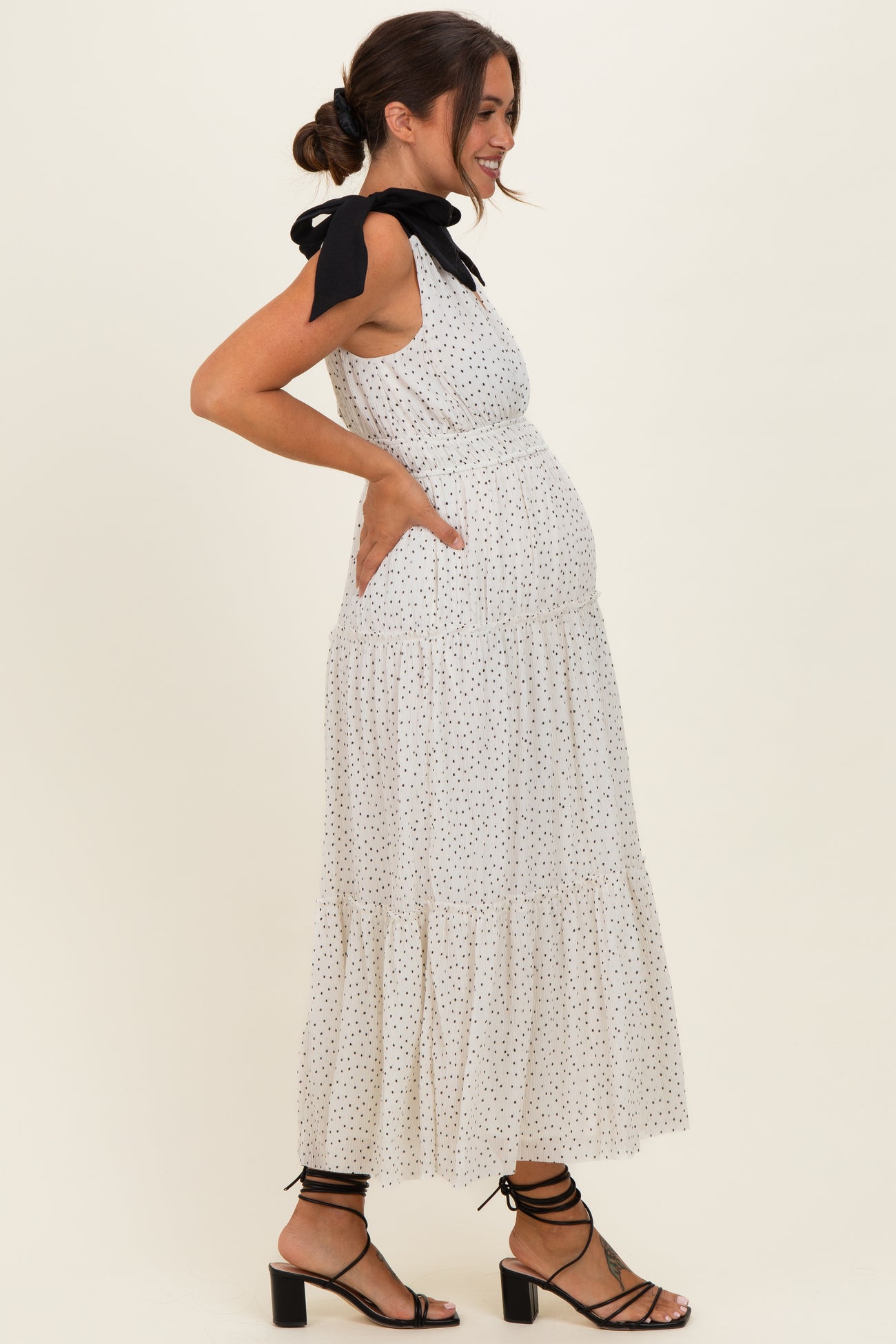 woman wearing a white polka dot maternity dress with a black bow detail and a visible baby bump