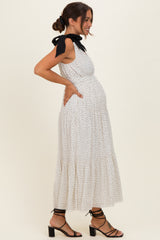 woman wearing a white polka dot maternity dress with a black bow detail and a visible baby bump