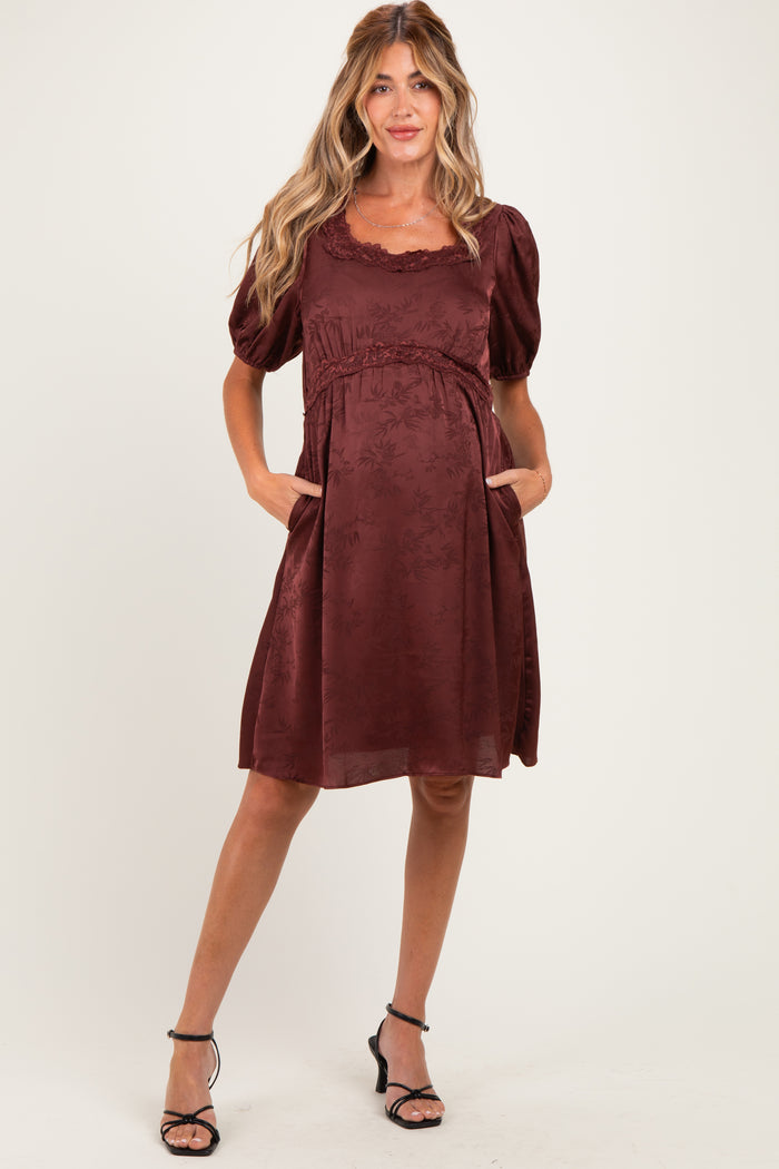 woman wearing a burgundy maternity dress with puff sleeves and pockets, showcasing a baby bump