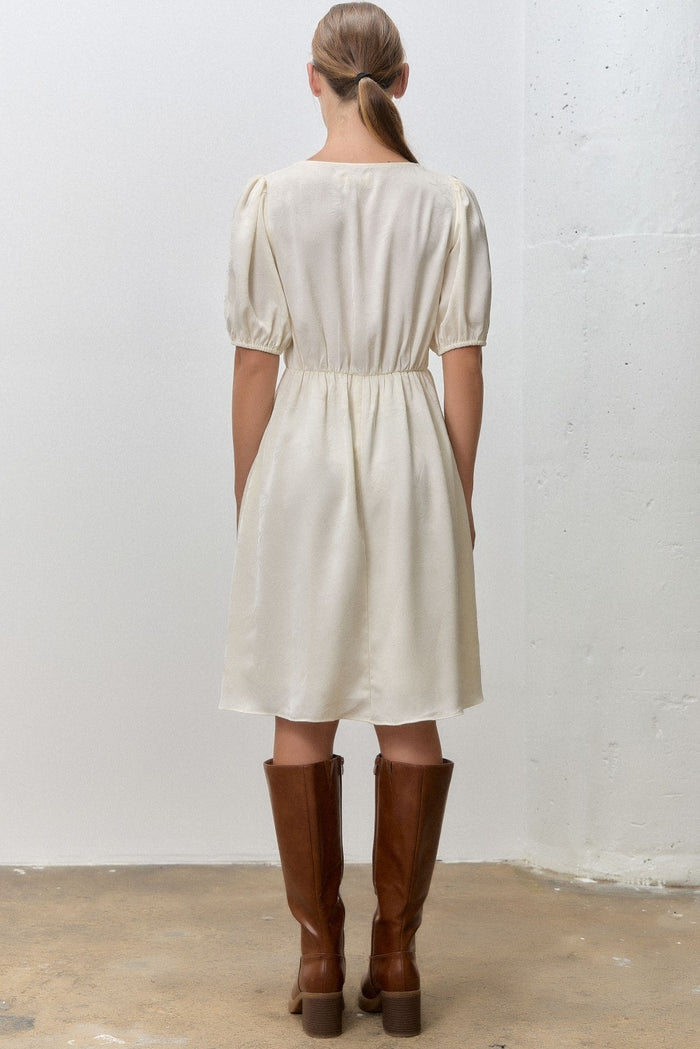 woman wearing a cream-colored short puff sleeve dress with a cinched waist and knee-high brown leather boots
