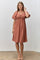 woman wearing a rust-colored puff sleeve dress with a square neckline and gathered detailing