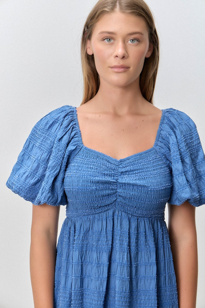 woman wearing a blue smocked dress with puff sleeves and a square neckline