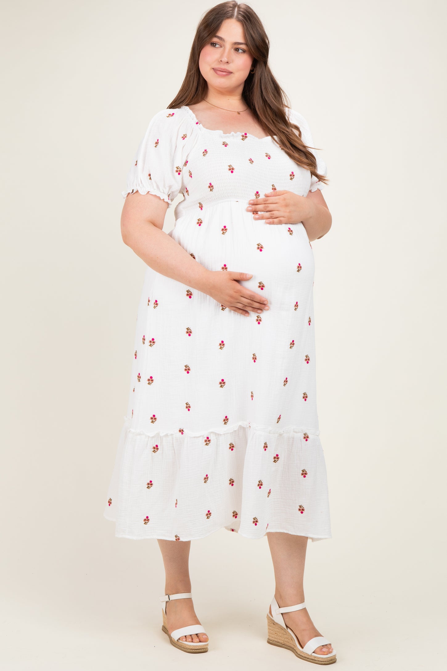 woman wearing a white maternity plus dress with floral print and ruffle hem, gently cradling her baby bump