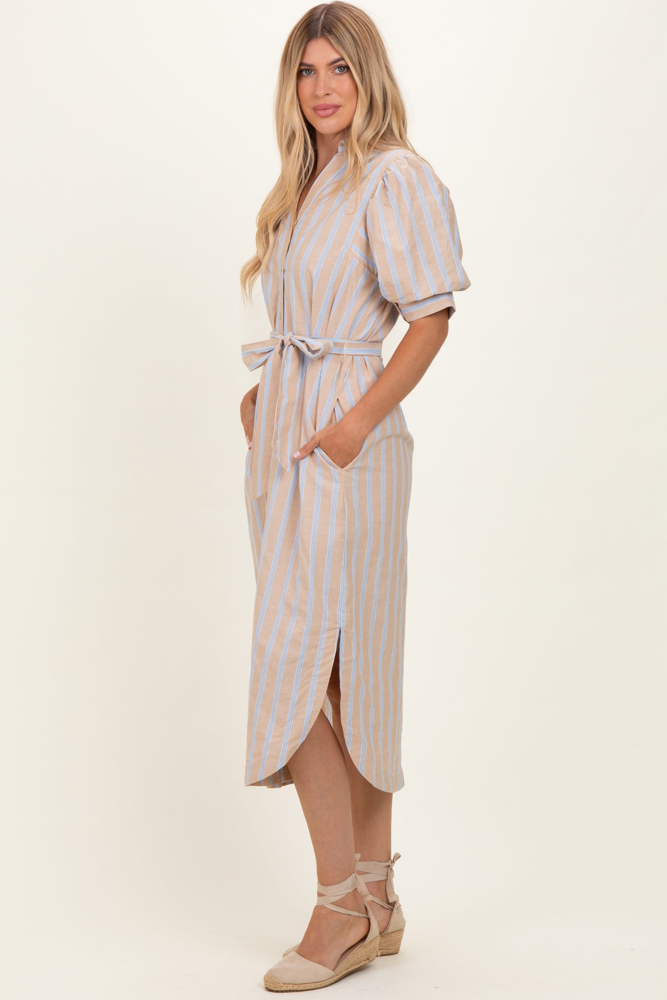 woman wearing a beige and blue striped maxi dress with puff sleeves and a tie belt, featuring side pockets and slits