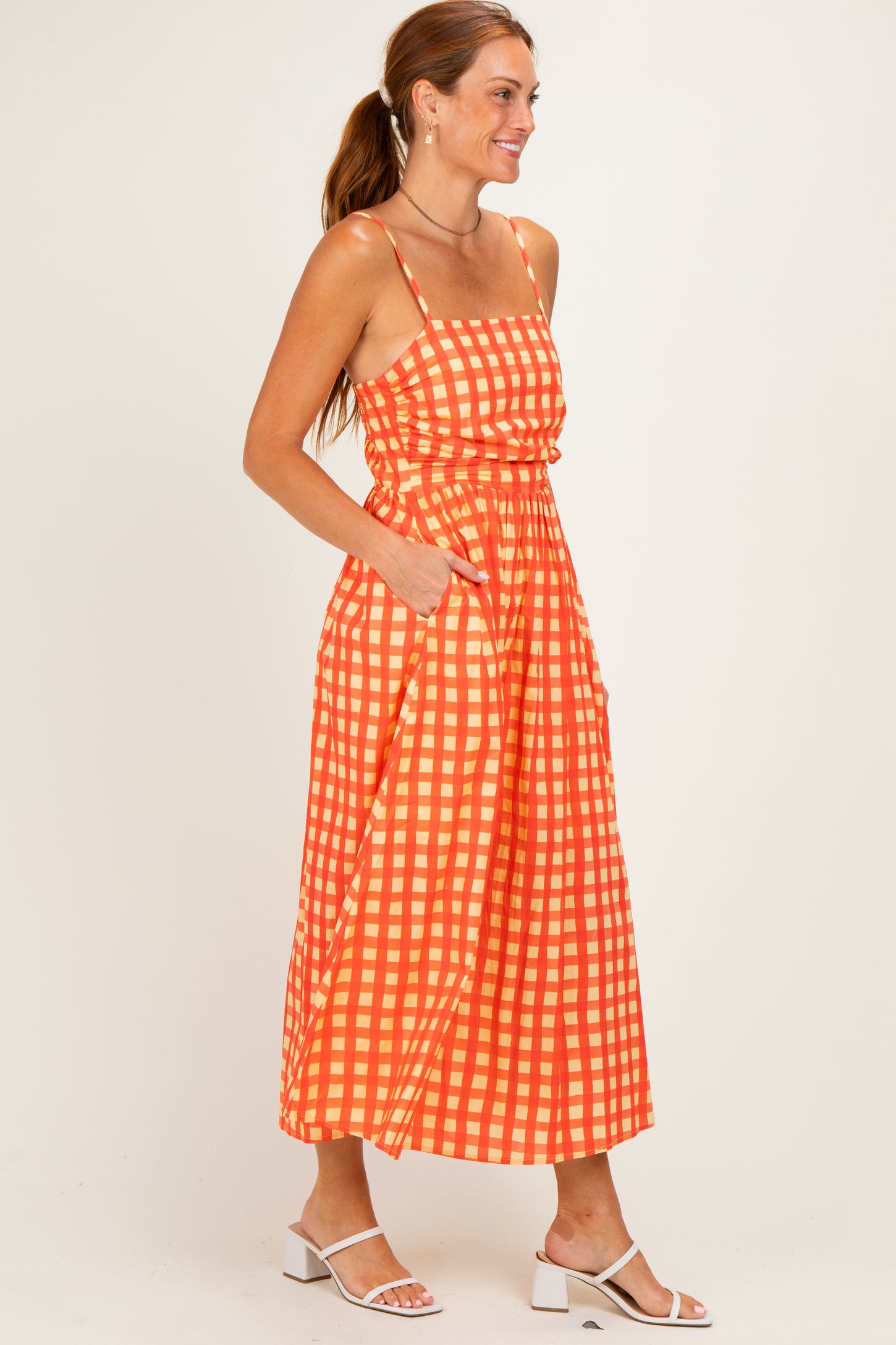 woman wearing a bright orange gingham midi dress with thin straps and pockets