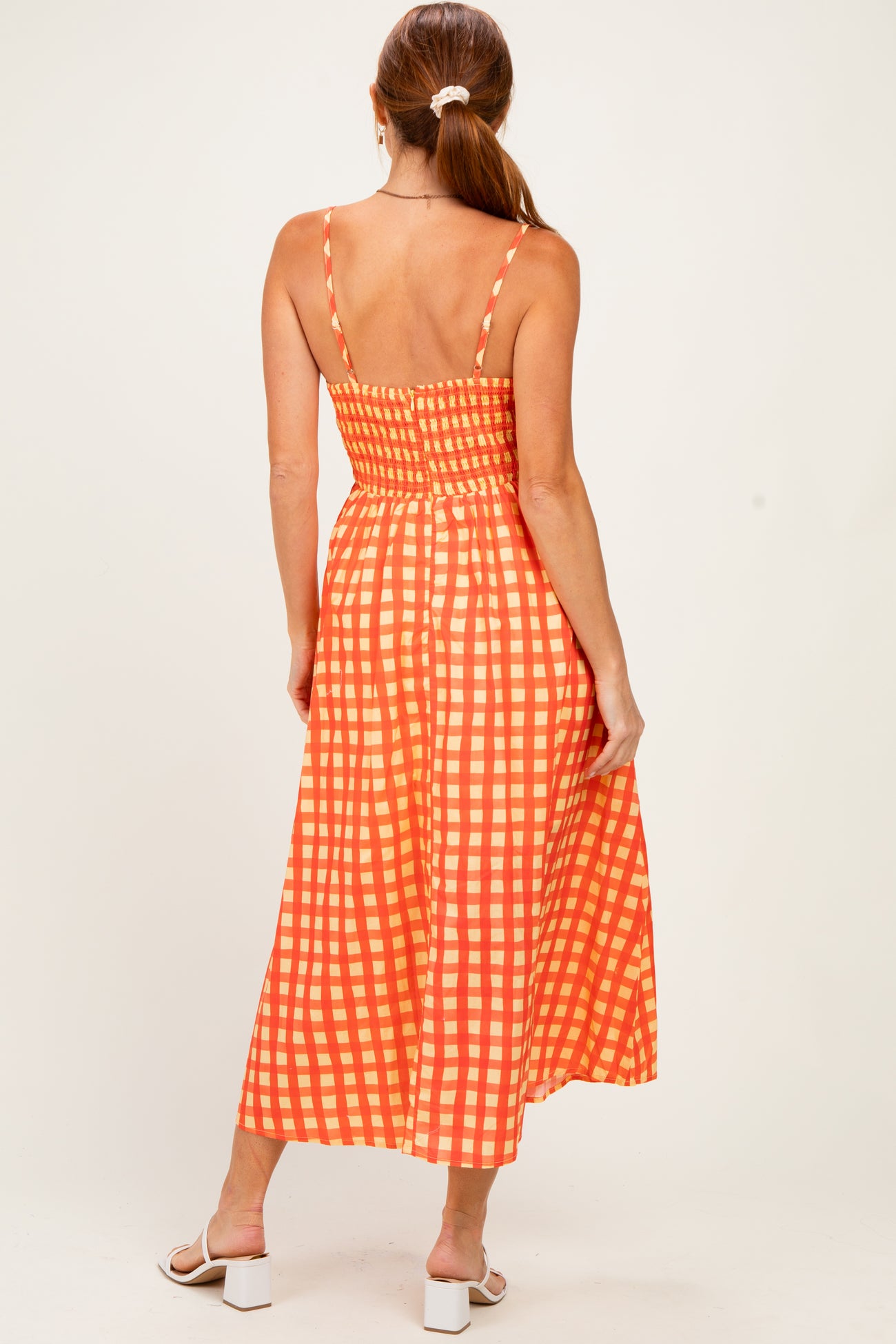 woman wearing an orange and white checked midi dress with a smocked back and thin straps