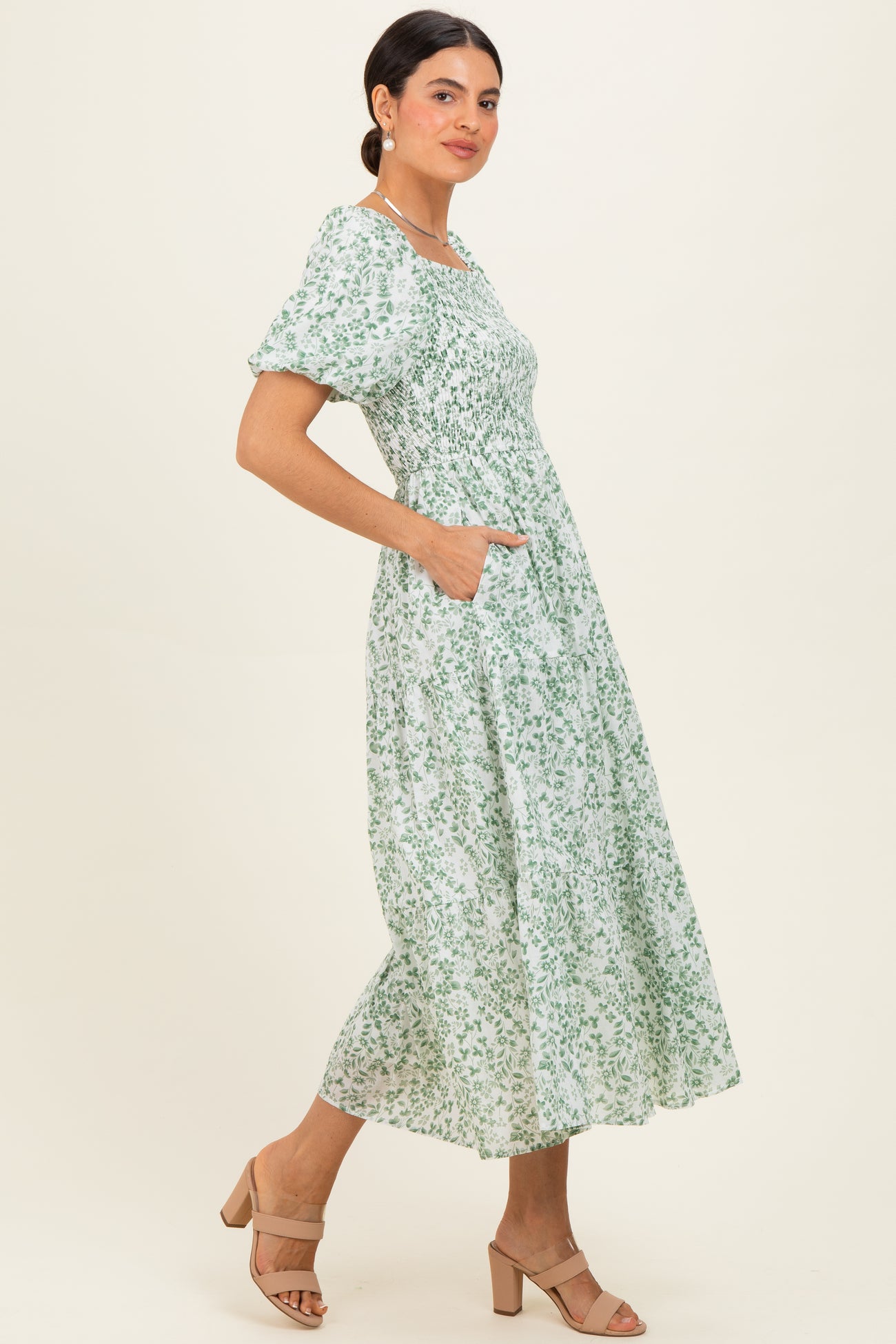 woman wearing a green floral midi dress with puff sleeves and pockets, standing in a relaxed pose