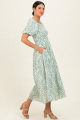 woman wearing a green floral midi dress with puff sleeves and pockets, standing in a relaxed pose