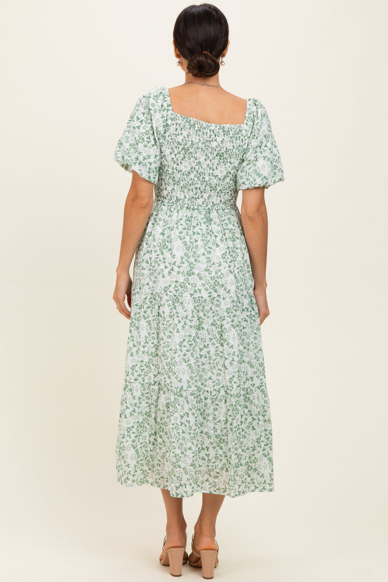 woman wearing a green and white floral midi dress with short puff sleeves and a smocked bodice, view from the back