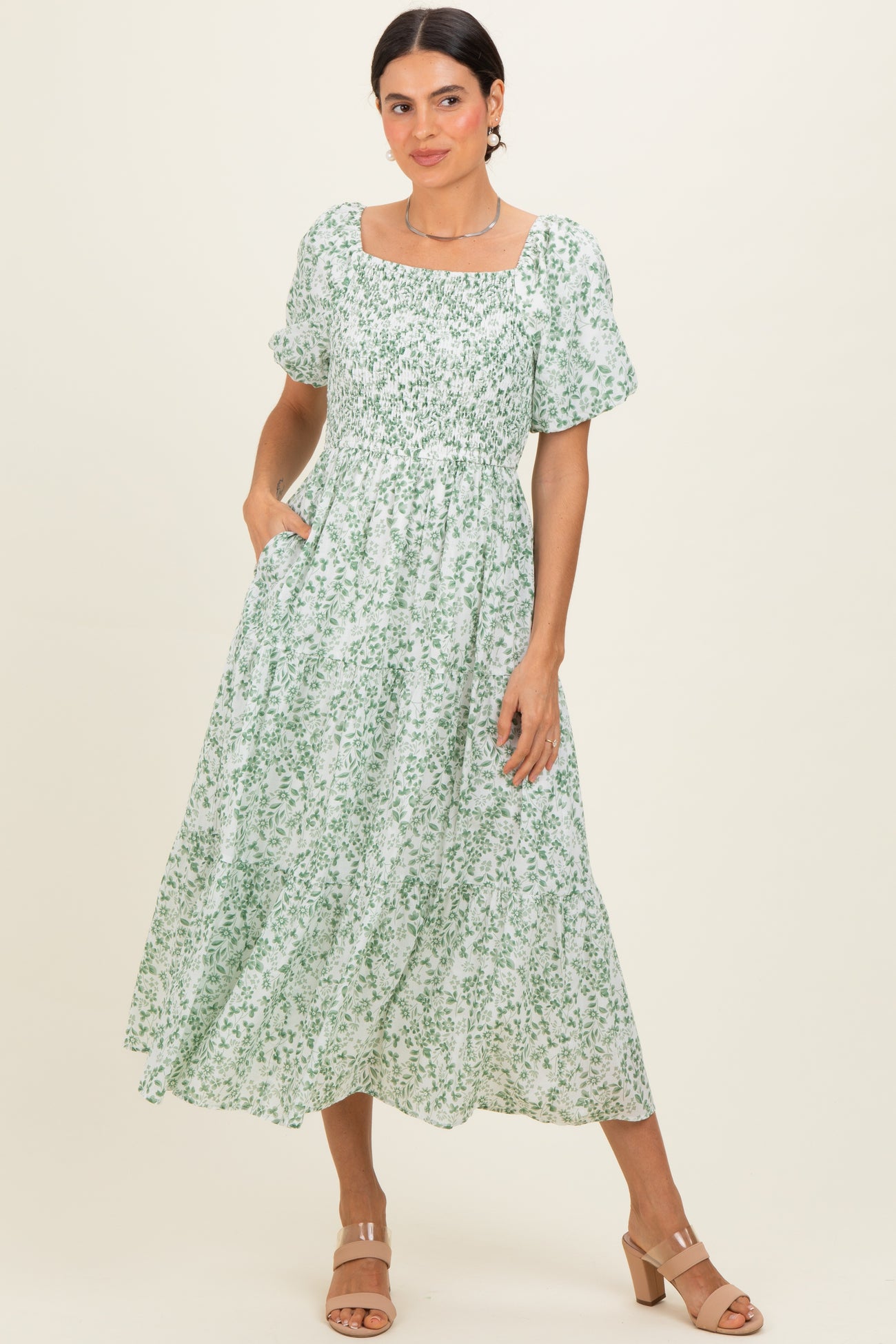 woman wearing a white floral maxi dress with puff sleeves and square neckline, standing with hands in pockets