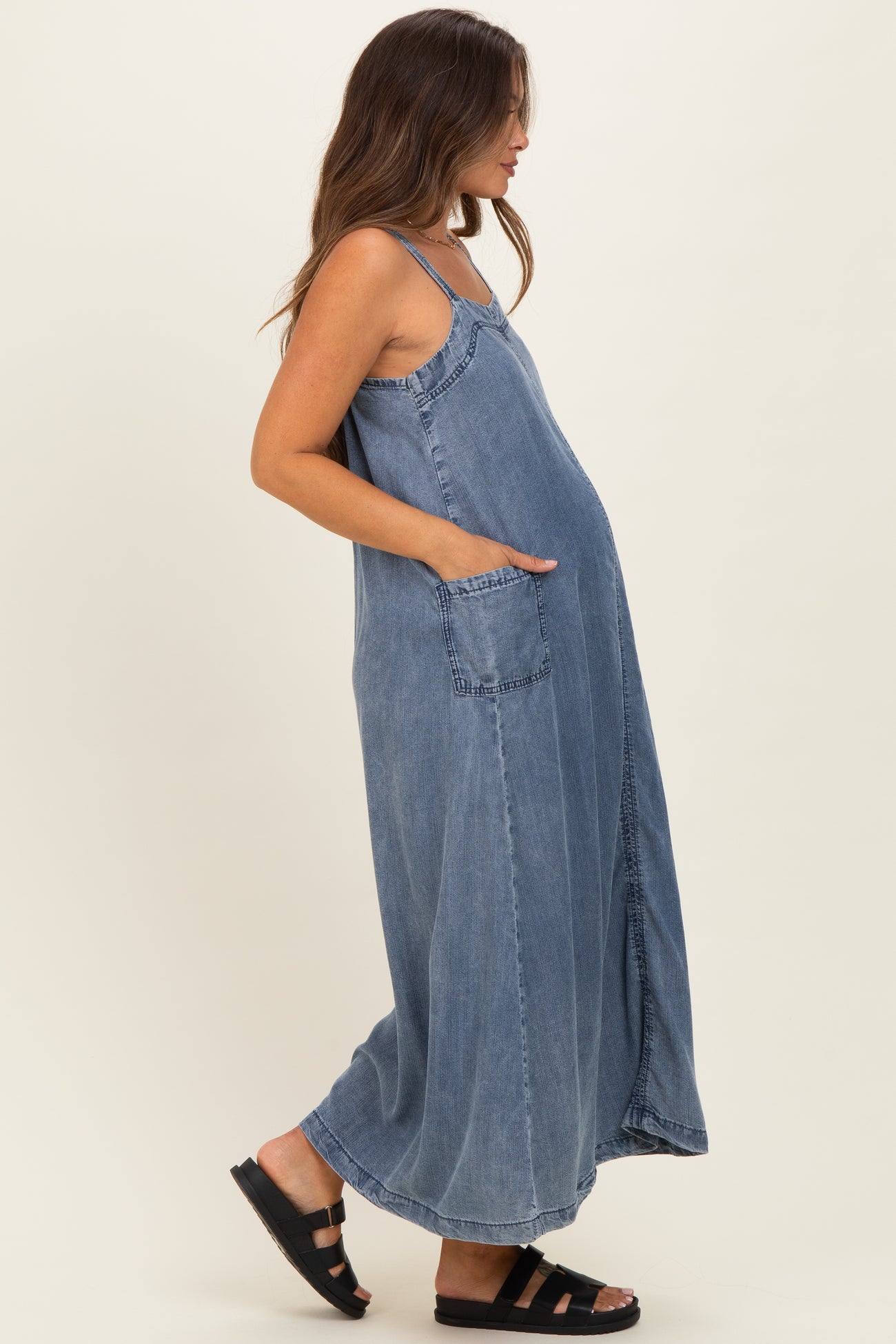 woman wearing a blue denim maxi maternity dress with pockets and a visible baby bump