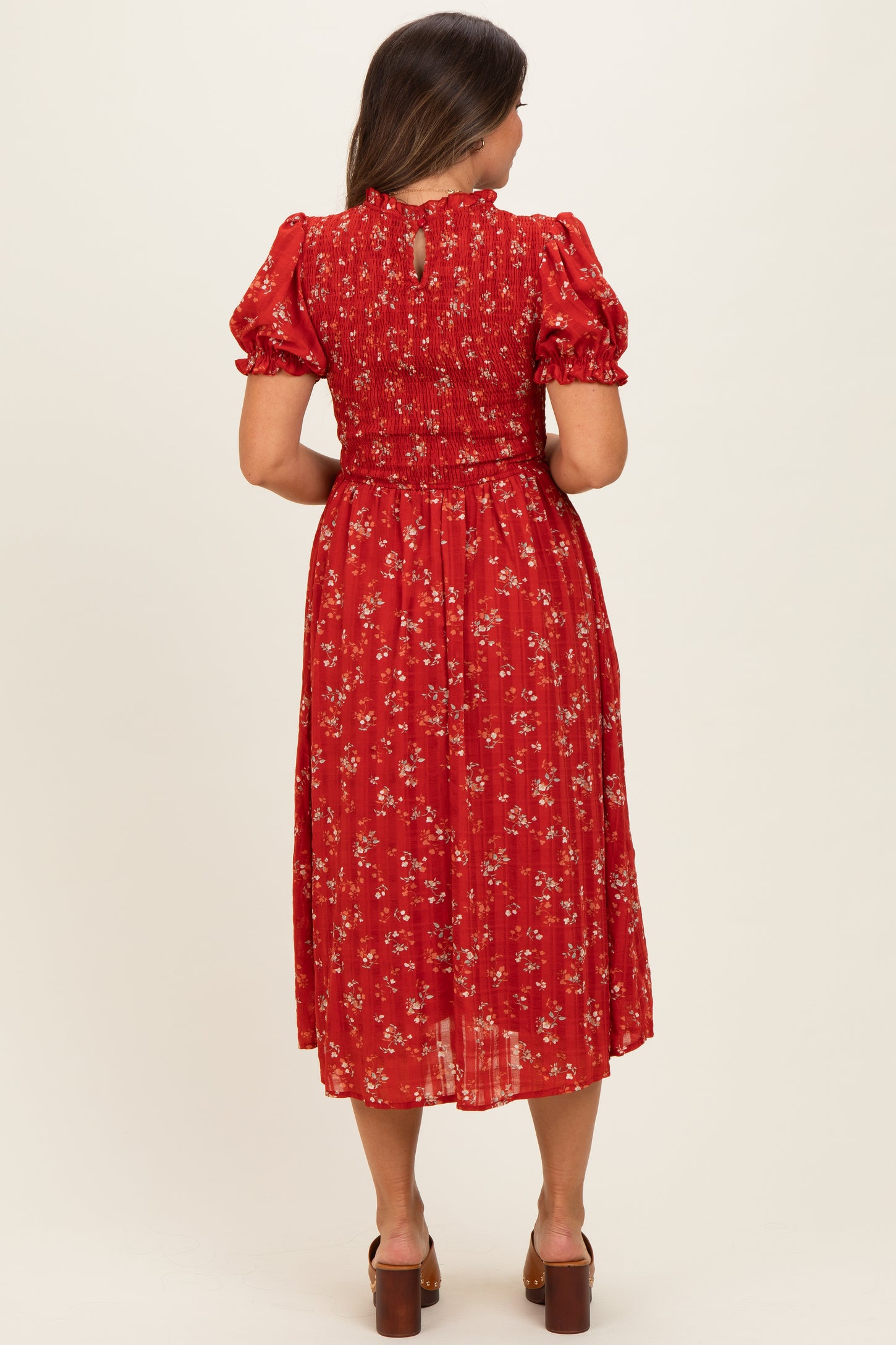 woman wearing a red floral maternity dress with puff sleeves and smocked back, showing a flowy mid-calf length