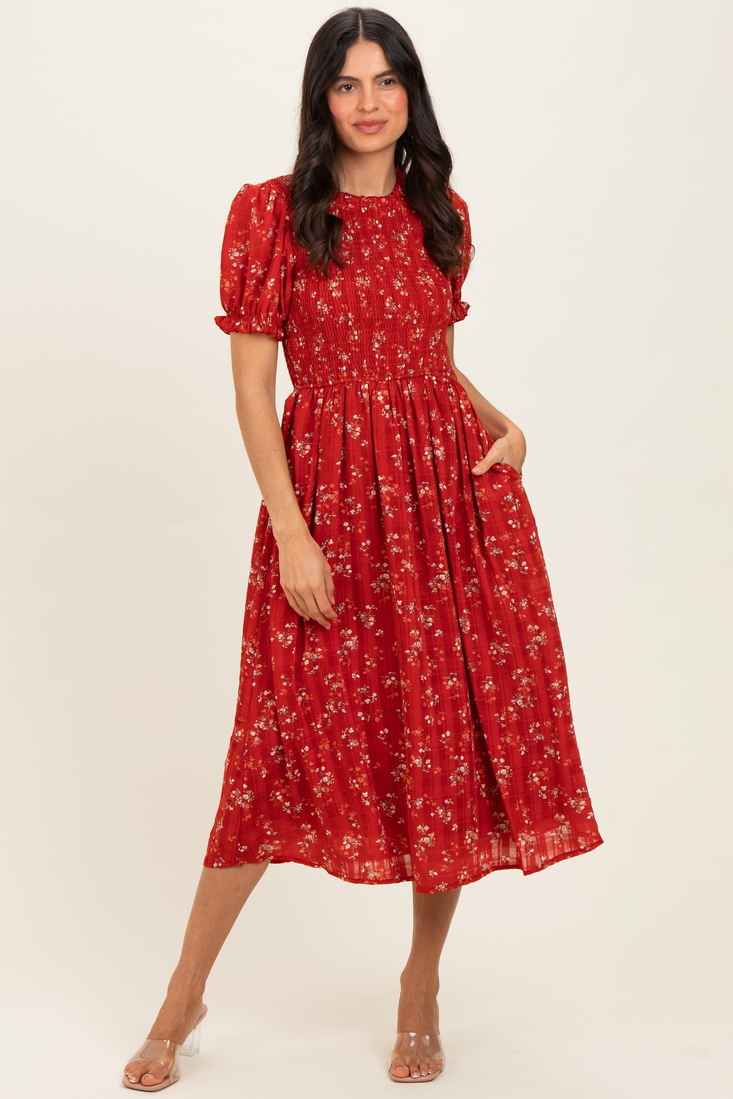 woman wearing a red floral midi dress with puff sleeves and a smocked bodice, posing with one hand in the pocket