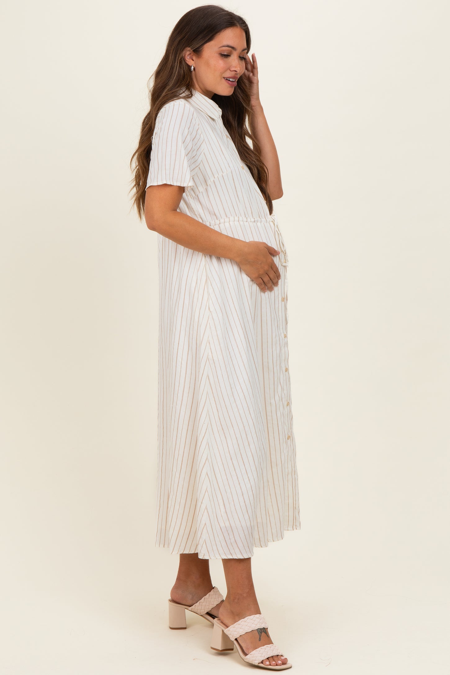 woman wearing a striped maternity dress with short sleeves and button details, gently holding her baby bump