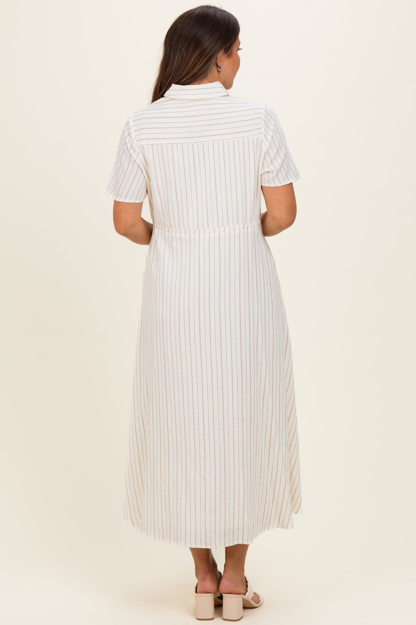woman wearing a white striped maternity dress with short sleeves and a fitted waist, showing the back view