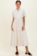 woman wearing a cream striped midi dress with short sleeves and a drawstring waist, paired with black slide sandals