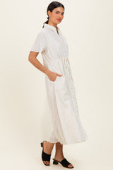 woman wearing a white and beige striped midi shirt dress with a tie waist and side pockets, standing in a relaxed pose