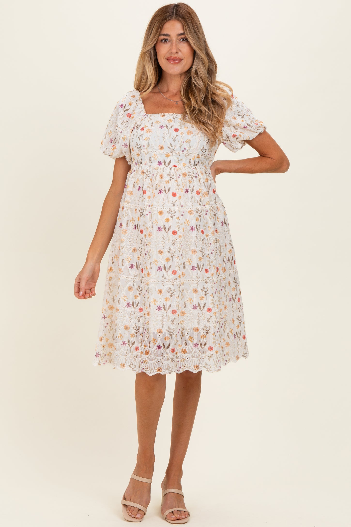 woman wearing a floral maternity dress with short puff sleeves and a square neckline, standing on a light background