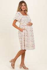 woman wearing a white floral maternity dress with short puff sleeves and pockets, gently cradling her baby bump