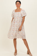 woman wearing a white floral embroidered short sleeve dress with a square neckline and puff sleeves