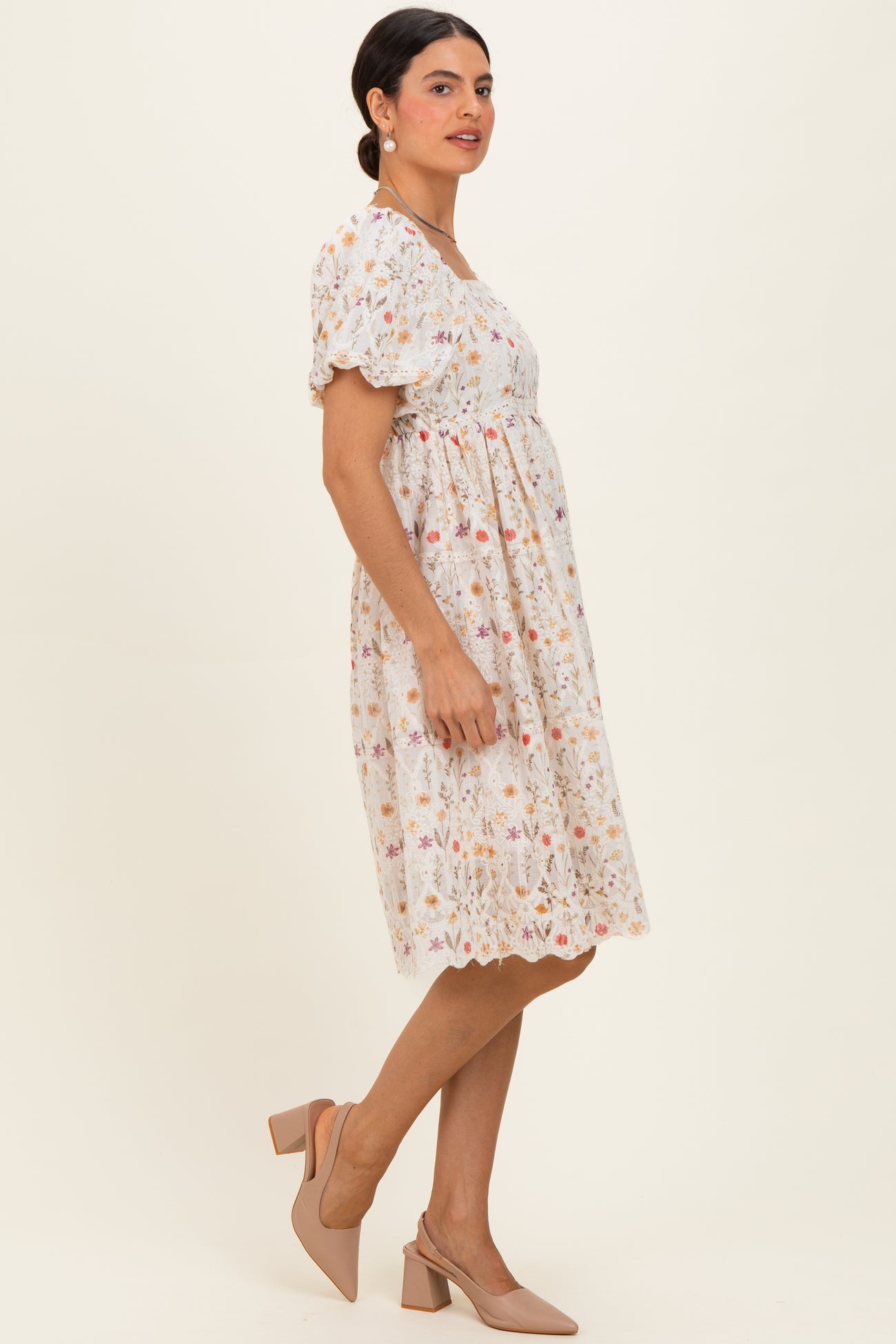 woman wearing a short sleeve white floral dress with a cinched waist and a flared skirt, paired with nude heels