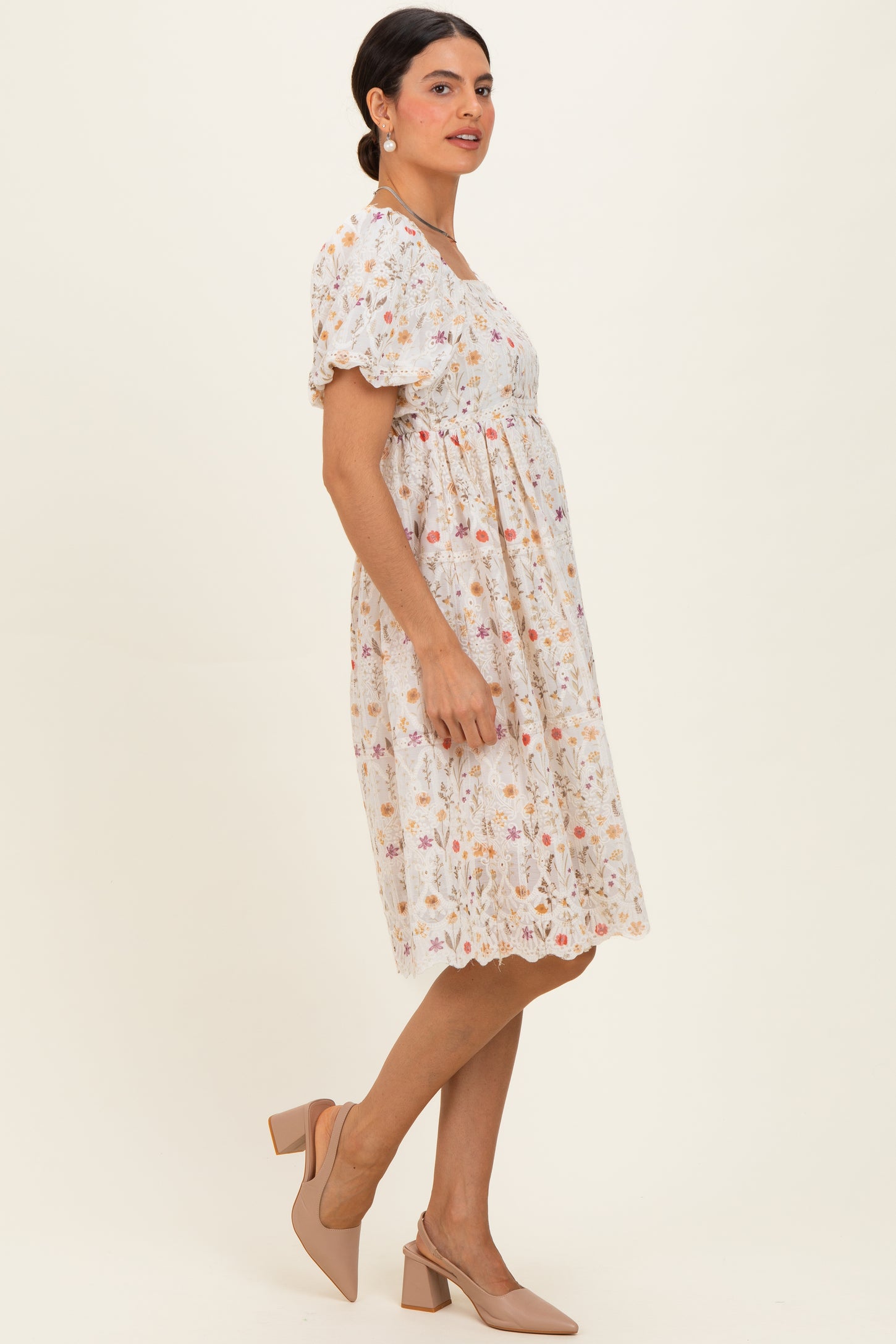 woman wearing a short sleeve white floral dress with a cinched waist and a flared skirt, paired with nude heels