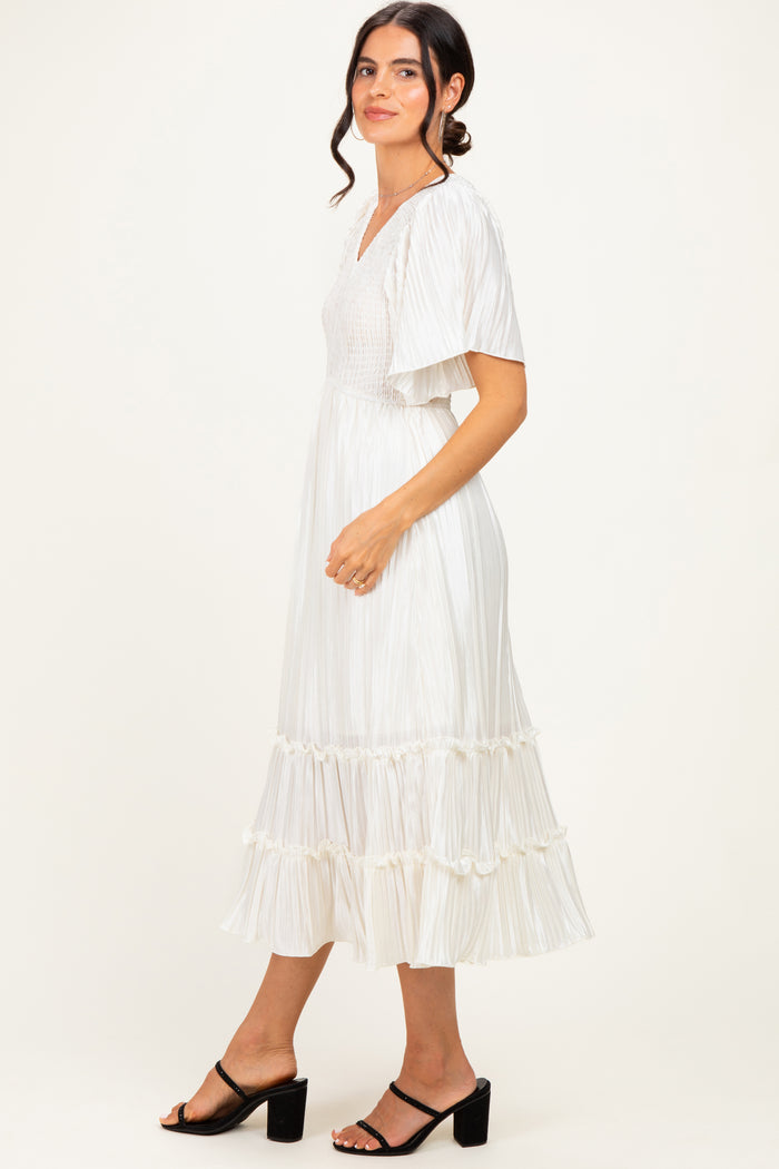 woman wearing a white pleated midi dress with flutter sleeves and ruffled hem, standing sideways with a smile