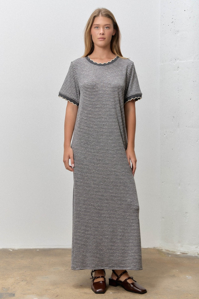 woman wearing a long striped grey maxi dress with scalloped edges and short sleeves