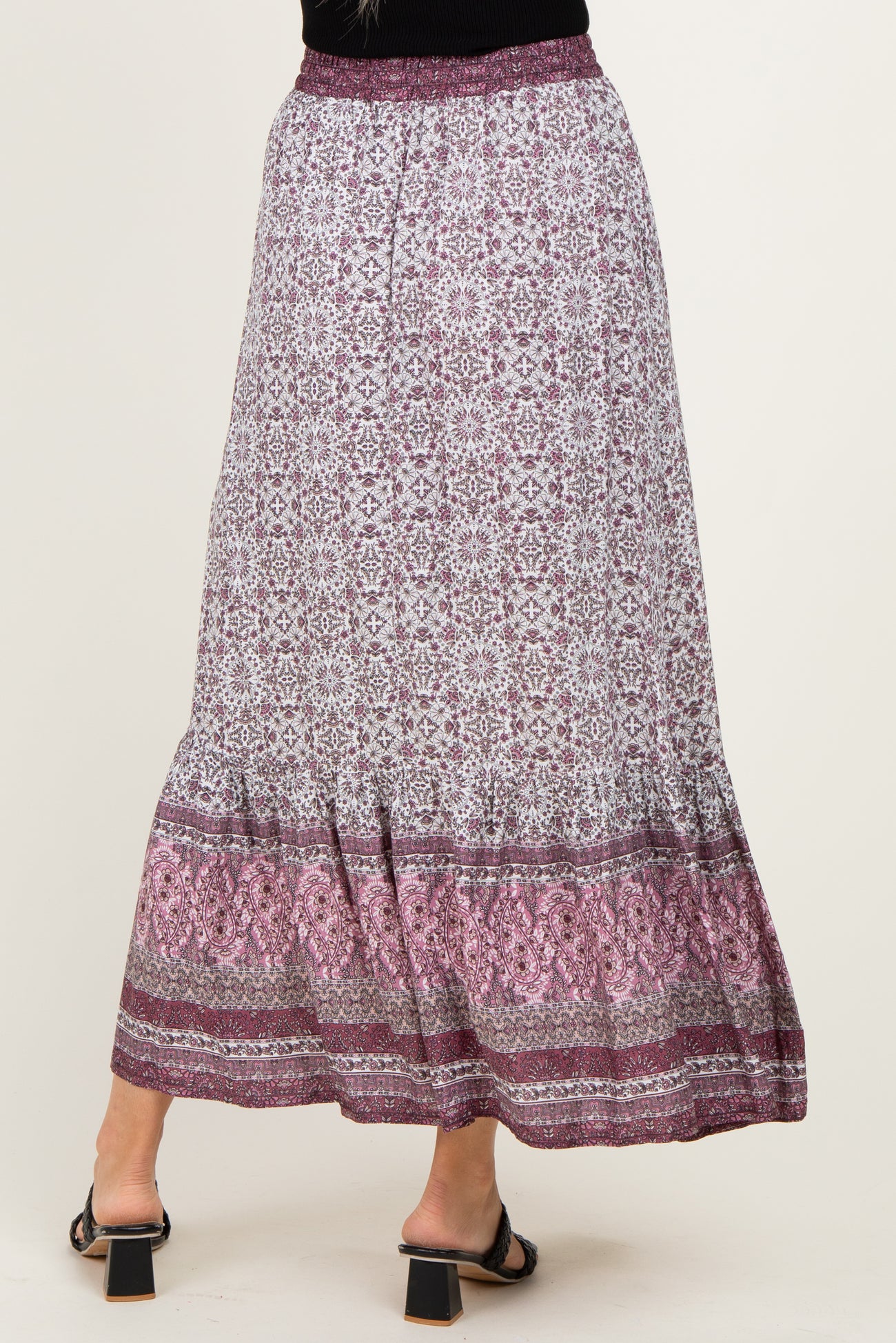 woman wearing a patterned maxi skirt with a tiered hem and a purple color palette, viewed from the back