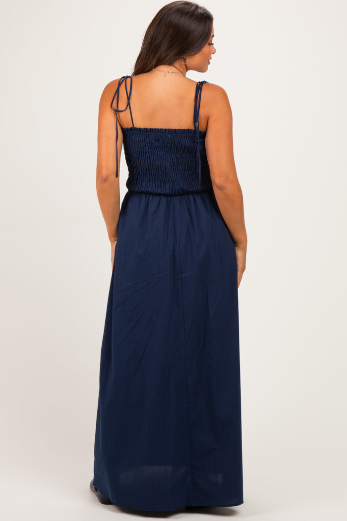 woman wearing a navy blue maternity maxi dress with a smocked bodice and adjustable straps, showing her back