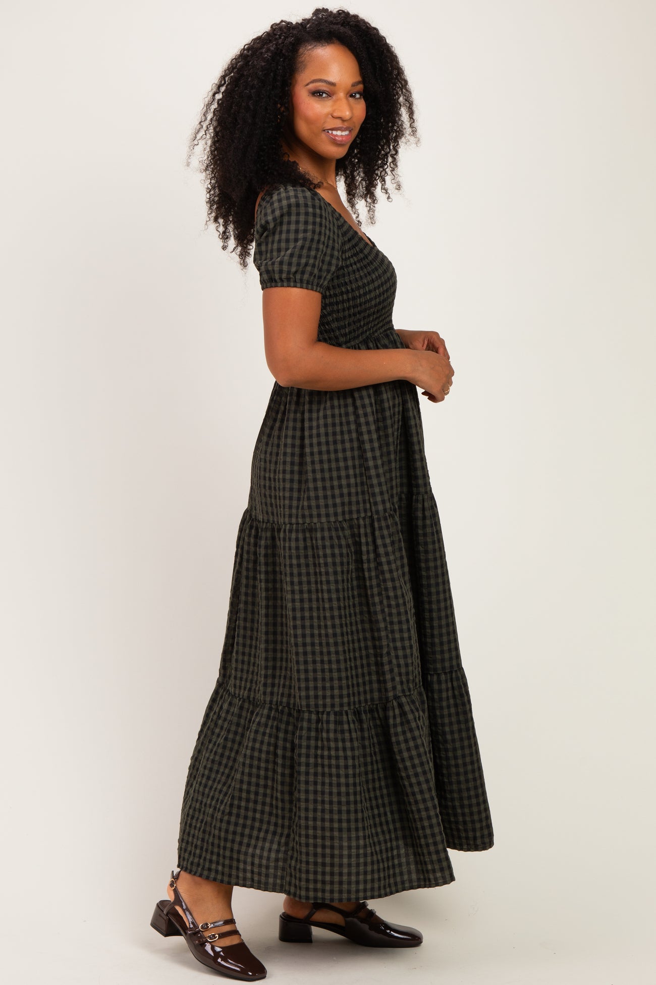woman wearing a dark green and black checkered maxi dress with short sleeves and tiered skirt, standing sideways