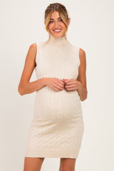 woman wearing a light beige sleeveless maternity dress with a ribbed turtleneck and cable knit design, showing her baby bump