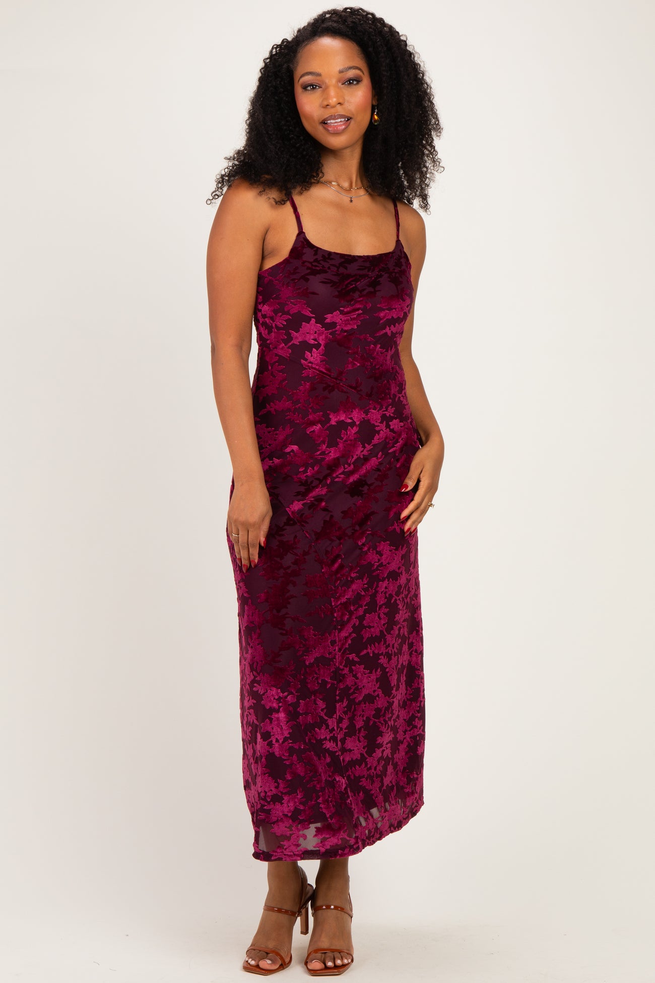 woman wearing a burgundy floral print spaghetti strap maxi dress with curly hair and a confident smile
